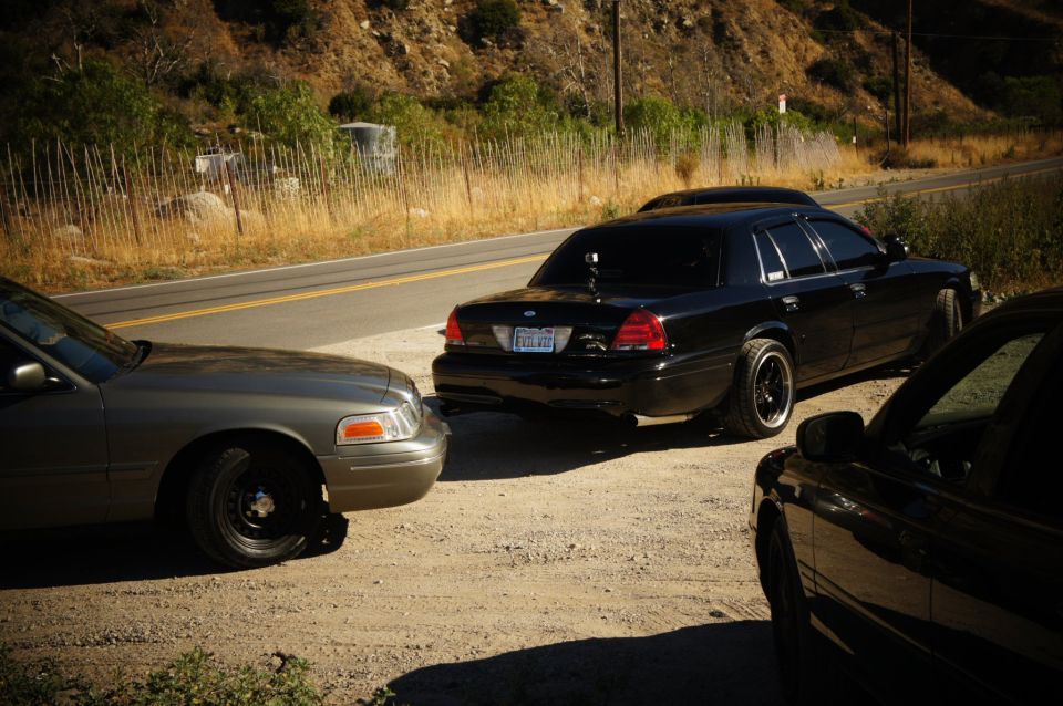 Black Ford Crown Victoria rear quarter parked on gravel beside a mountain road