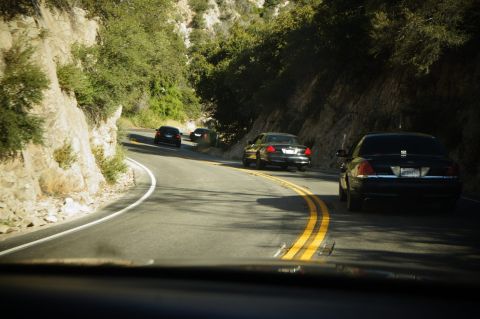 2003 Ford Crown Victoria - Convoy of dark sedans tracking a double-yellow curve through a wooded canyon.