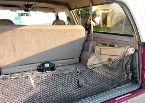 1994 Ford Bronco - Rear cargo area of a tan-interior Ford SUV shot through the open tailgate, with a black stretch cargo net stretched across the carpeted flo…