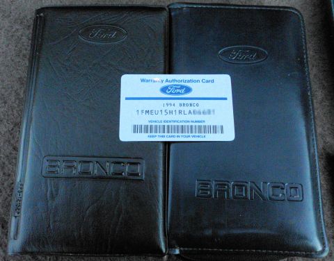 1994 Ford Bronco - Two black embossed Ford "BRONCO" owner's-manual vinyl pouches laid side by side on gray carpet, with a Ford Warranty Authorization Card bet…