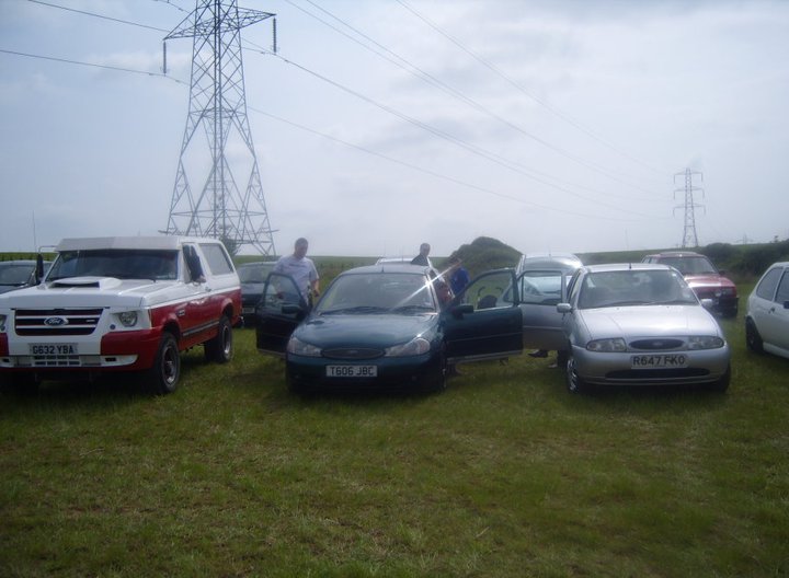 White and red Ford Bronco parked in a grassy field with other cars and people
