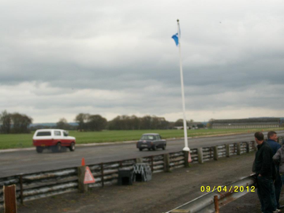 Red and white SUV with a camper shell driving on a track, dark sedan follows