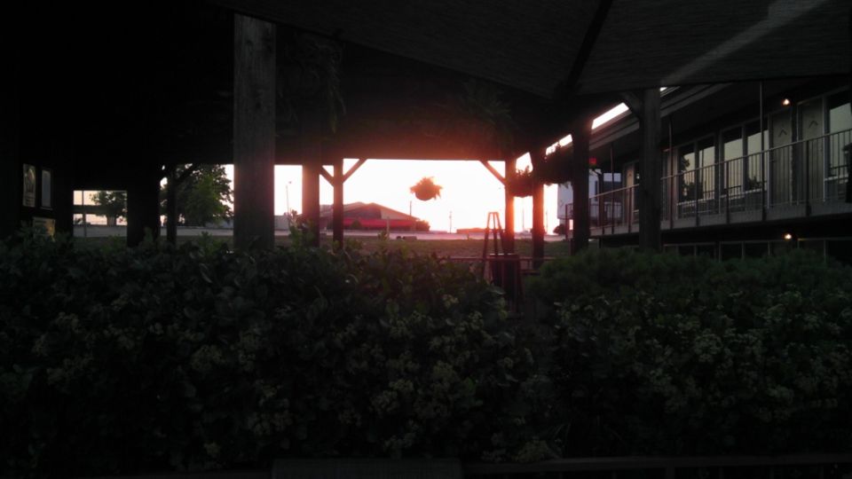 Red car visible in the distance during sunset, framed by a covered structure