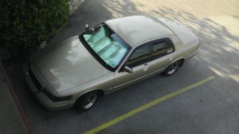 2000 Mercury Grand Marquis - A tan 2000 Mercury Grand Marquis is parked in a lot, with sunshades on the windshield.