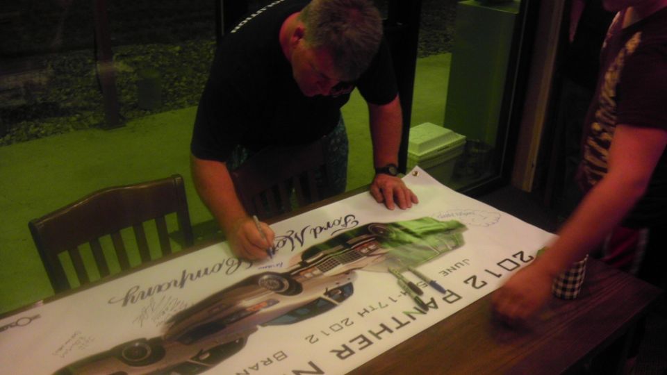 Man signing a 2012 Panther Nationals event banner laid on a table