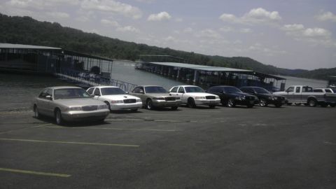 2000 Mercury Grand Marquis - Multiple vehicles are parked in a lot next to a lake with covered docks in the background.