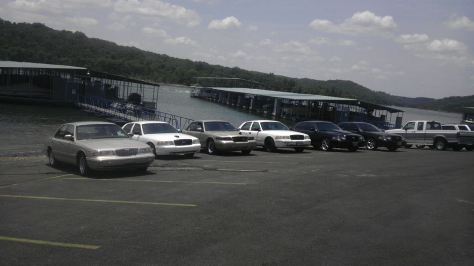 Several sedans and pickup trucks parked in a lot near a lake with docks