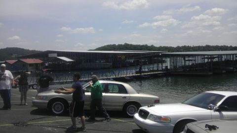 2000 Mercury Grand Marquis - A silver sedan is parked near a body of water with a large marina structure behind it.