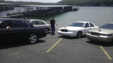 2000 Mercury Grand Marquis - Several sedans are parked near a lake with a marina in the background.