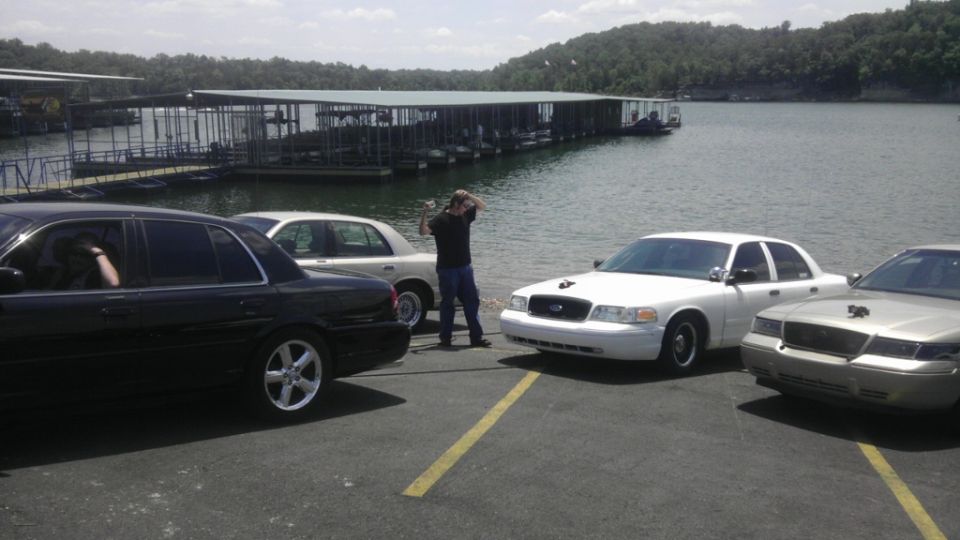 Four sedans, one black, one white, one tan, and one silver, parked near a lake with docks