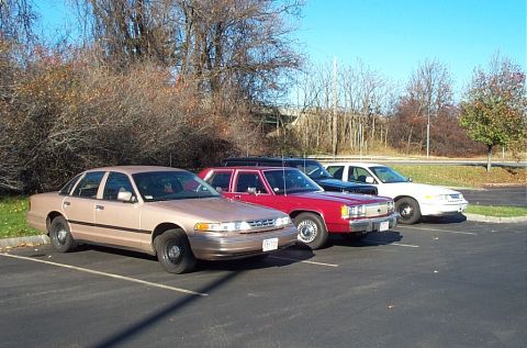 1991 Ford LTD Crown Victoria - A row of sedans, including a tan 1991 Ford Crown Victoria LTD, are parked in a lot on a clear day.