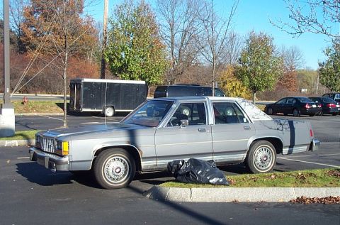 1991 Ford LTD Crown Victoria - A gray 1980s Ford Crown Victoria is parked in a lot with a black trailer nearby.