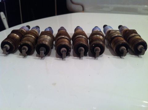 2001 Mercury Grand Marquis - A set of eight used spark plugs are laid out on a white surface, showing signs of wear.