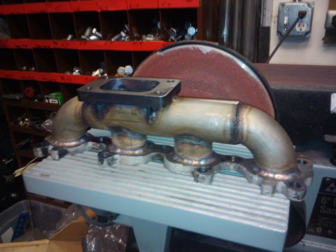 1995 Ford Probe - A custom turbo exhaust manifold sits on a workbench, ready for installation or modification.