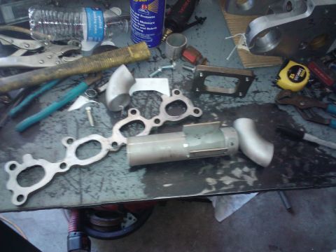 1995 Ford Probe - Various exhaust manifold components and tools are laid out on a workbench, suggesting a repair or modification in progress.