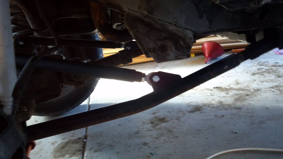Underside view of a vehicle's suspension and frame components. A red funnel is visible in the background