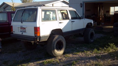 1995 Jeep Cherokee - A white 1995 Jeep Cherokee, modified with oversized tires, is seen parked outdoors next to another vehicle.