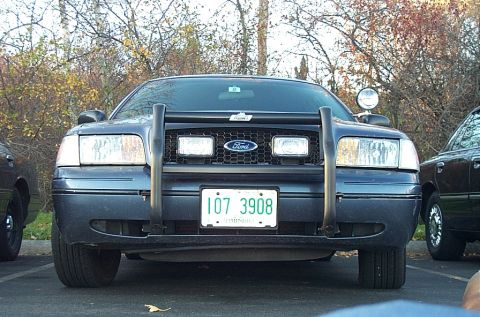 1991 Ford LTD Crown Victoria - Front view of a police car with a push bar and auxiliary lights, parked next to another vehicle.
