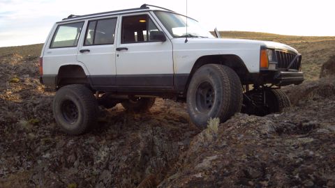 1995 Jeep Cherokee - A white Jeep Cherokee navigates a rocky, off-road path under a clear sky.