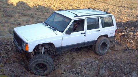 1995 Jeep Cherokee - A white 1995 Jeep Cherokee is shown traversing a challenging, rocky off-road path.