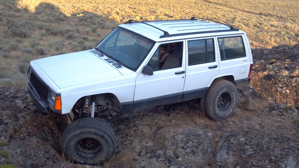 White 1995 Jeep Cherokee with lifted suspension and off-road tires navigating rocky terrain