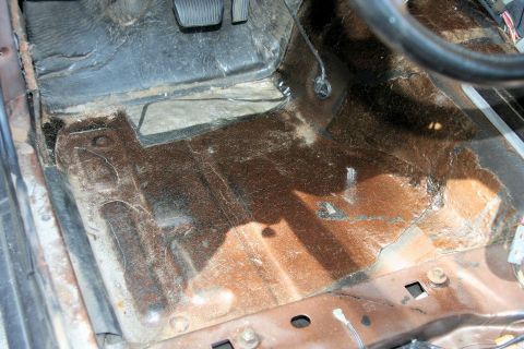 1980 Ford Mustang - The interior floor of a vehicle shows significant rust and damage, indicating a need for restoration.