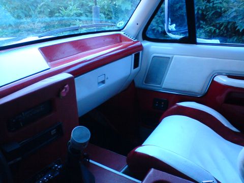 1989 Ford Bronco - The interior of a vehicle features two-tone red and white seats and matching dashboard accents.