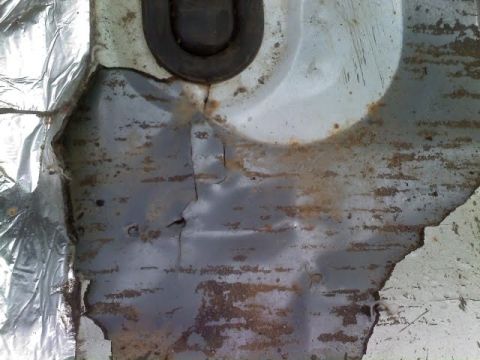 1996 Ford Bronco - Close-up view of a corroded metal panel, possibly from a vehicle's undercarriage, with damaged insulation material.