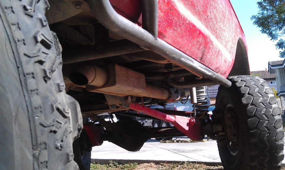 Undercarriage of a red off-road vehicle showing suspension, exhaust, and large tire