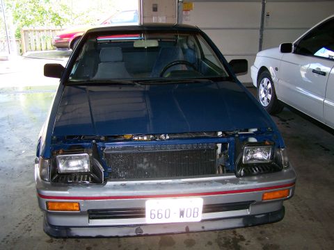 1988 Suzuki Samurai - Front view of a blue car with damage to its front end, including missing headlights and grille.