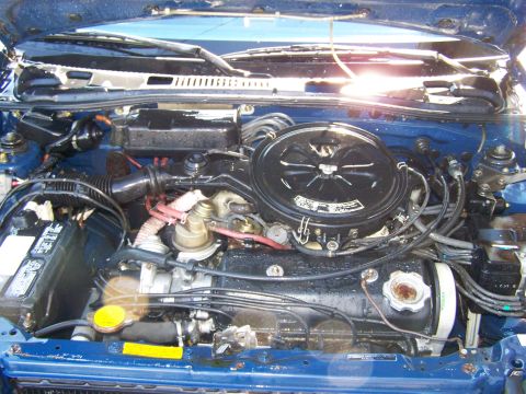 1988 Suzuki Samurai - The engine compartment of a blue vehicle is shown, various hoses, the battery, and the air filter assembly.