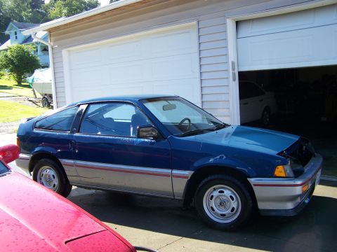1988 Suzuki Samurai - A blue Honda CRX is parked outside a garage, with a red car partially visible in the foreground.