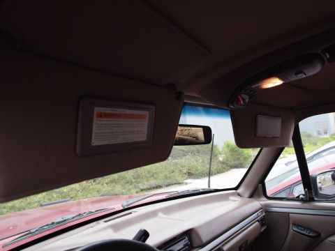 1994 Ford Bronco - The interior of a red vehicle is captured, highlighting the sun visors and dashboard, with a reflection in the rearview mirror.