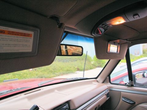 1994 Ford Bronco - The interior of a vehicle shows sun visors and a dashboard, with a reflection in the rearview mirror.