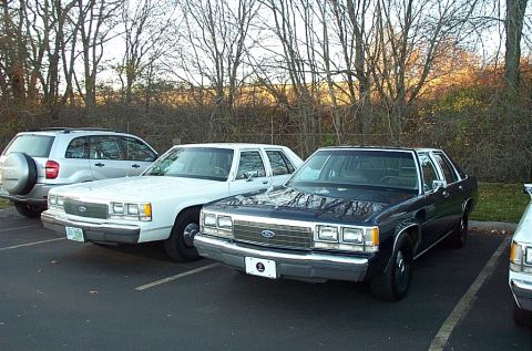 1991 Ford LTD Crown Victoria - Two Ford Crown Victorias and a silver SUV are parked in a lot on a fall day.