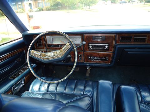 2001 Ford Crown Victoria - The interior of a car features blue leather seats and a wood-accented dashboard with a radio and gauges.