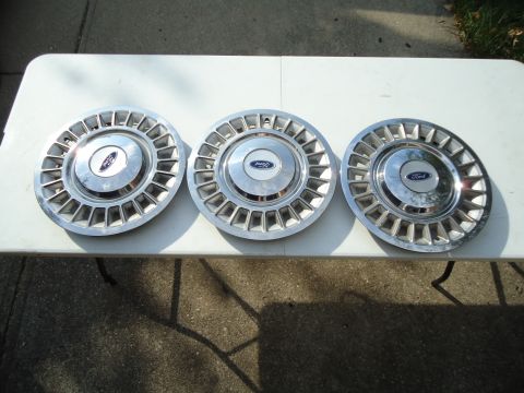 2001 Ford Crown Victoria - Three Ford hubcaps are displayed on a white surface. The hubcaps feature a chrome finish and a distinctive pattern of rectangular openings…