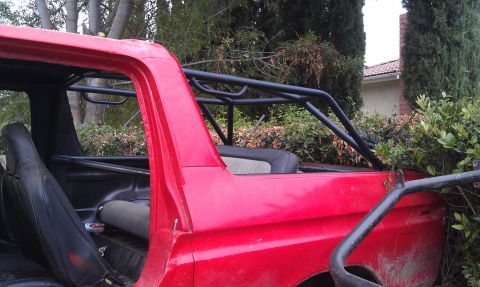 1978 Ford Bronco - This red SUV has been modified with a prominent black roll cage, suggesting off-road use.