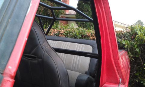 1978 Ford Bronco - Interior view of a red vehicle, showing bucket seats and a roll cage, with foliage visible through the open door.