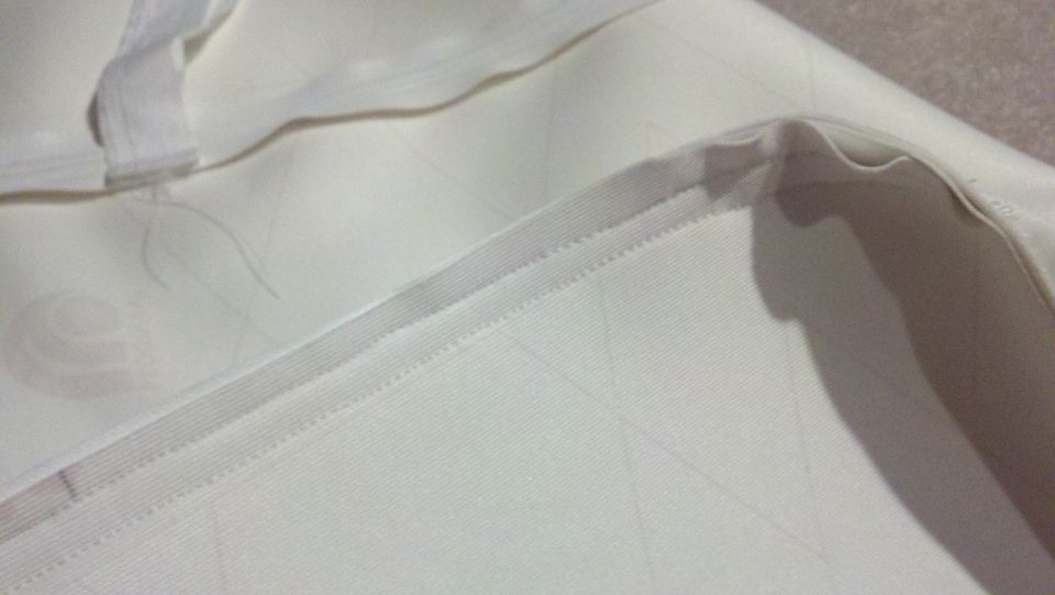 Close-up of white fabric with stitching and a subtle pattern. A Supermotors logo is visible in the corner