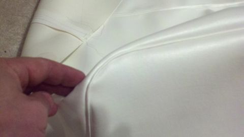1900 Ford C-350 (Centurion Conversions) - Close-up of white interior upholstery with visible stitching and a hand lifting a corner.