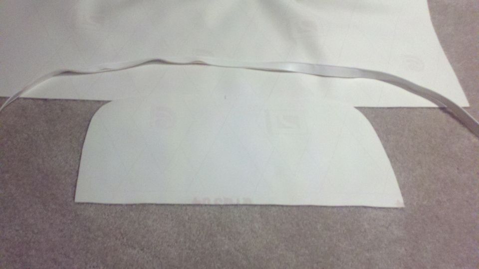 White fabric piece with a curved edge and a thin strap across it