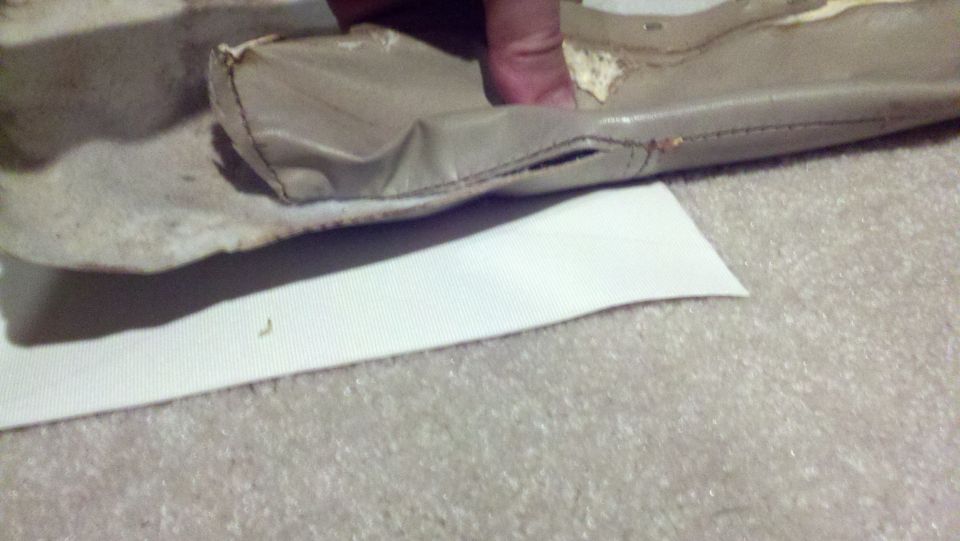 Torn beige upholstery with visible stitching and foam, resting on a white surface over carpet