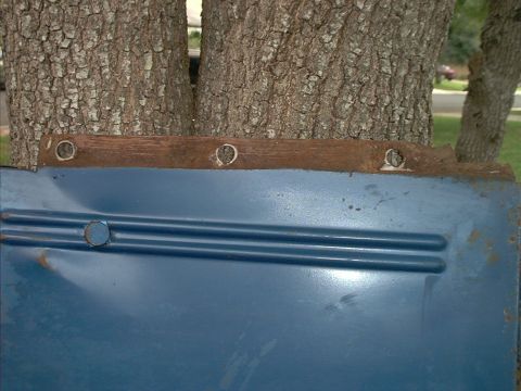 1971 Ford Bronco - A blue metal panel, possibly a door or fender, shows signs of wear and rust, with a wooden strip bolted to its upper edge.