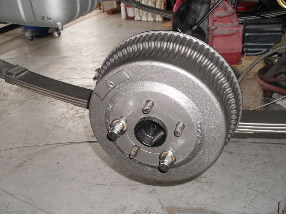 Refinished gray rear brake drum with new wheel studs on a leaf-spring axle in a shop