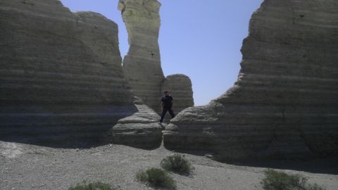 1989 Ford Bronco - A person is dwarfed by towering, layered rock formations in a desert landscape.