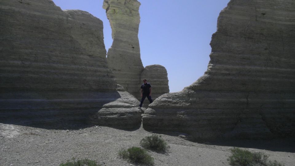 Person stands between layered rock formations under a clear blue sky