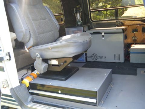 1988 Ford E350 - The interior of a van is shown, a swivel seat, a portable refrigerator, and storage compartments.
