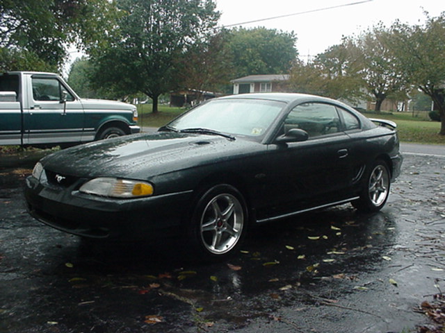 Dark green coupe with spoiler, 3q front view. Appears to be a 1994 Ford Mustang