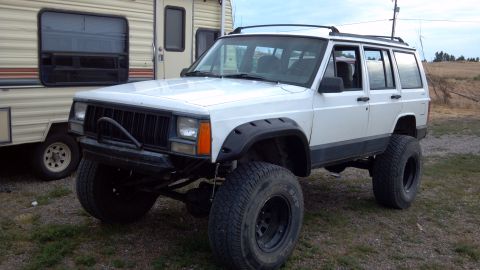 1995 Jeep Cherokee - Modified 1995 Jeep Cherokee with large tires and aftermarket bumper sits next to an RV.